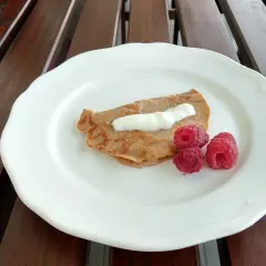 Naleśnik z mąki kasztanowej z jogurtem i malinami na białym talerzu.