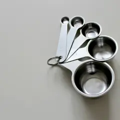 Zestaw metalowych miarek kuchennych o różnych rozmiarach, ułożonych na jasnym tle.