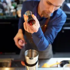 Barman przelewa czerwony płyn z jiggera do shakera.