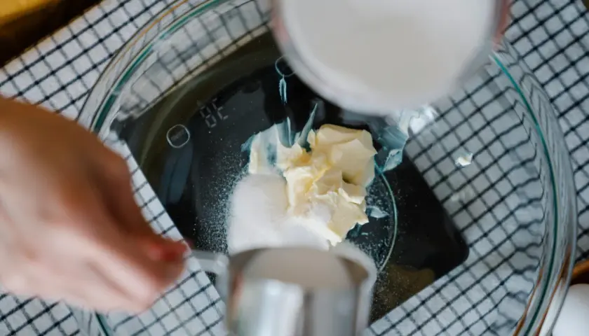 Kobieta wsypuje cukier do miski z masłem na wadze kuchennej.